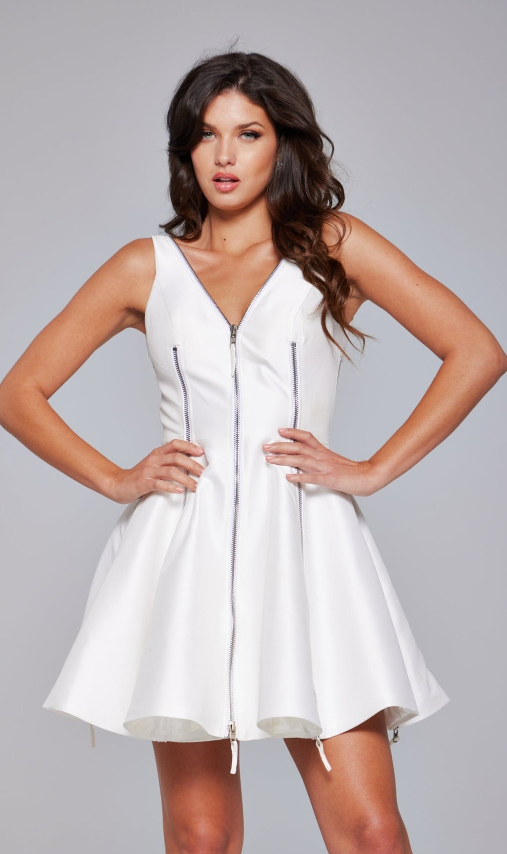 A woman poses with hands on hips in the Jovani 39821 Short A-Line White Hoco Dress, featuring sleeveless styling and front zipper accents, set against a plain background.